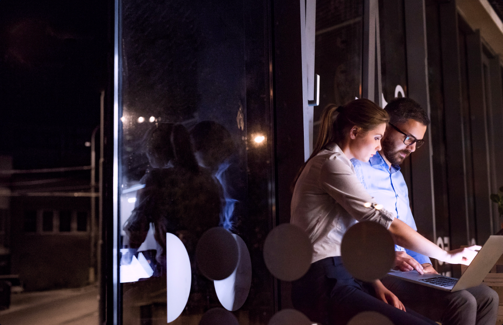 Two professionals reviewing data on a laptop at night